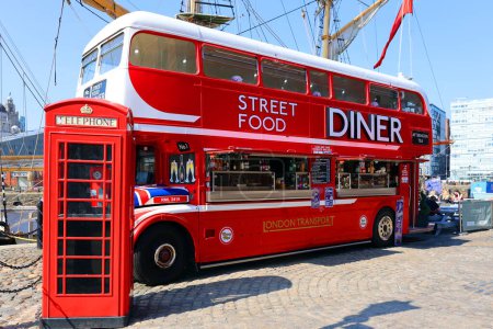 Photo for LIVERPOOL UNITED KINGDOM 06 07 2023: Red food double decker bus offering street food in Albert Dock with tables and a red telephone - Royalty Free Image