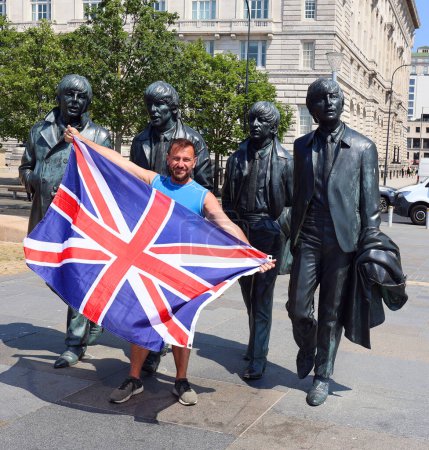 Photo for LIVERPOOL UNITED KINGDOM 06 07 20: Man with british flag in front The Beatles statue on Liverpool's Waterfront in 2015. Donated by the famous Cavern Club - Royalty Free Image