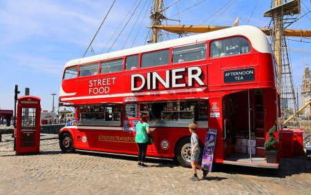 Photo for LIVERPOOL UNITED KINGDOM 06 07 2023: Red food double-decker bus offering street food in Albert Dock with tables and a red telephone - Royalty Free Image