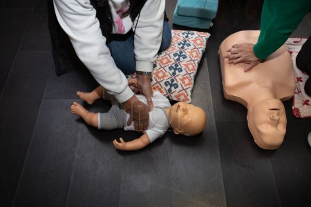 Photo for Three people practice first aid and CPR with an adult CPR manikin and another baby resuscitation manikin - Royalty Free Image