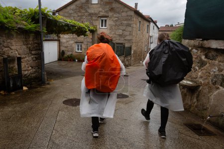 Photo for Three pilgrims walk the Portuguese Camino de Santiago on a rainy day. They pass through Pontecesures - Royalty Free Image