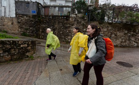 Photo for Three pilgrims walk the Portuguese Camino de Santiago on a rainy day. They pass through Pontecesures - Royalty Free Image