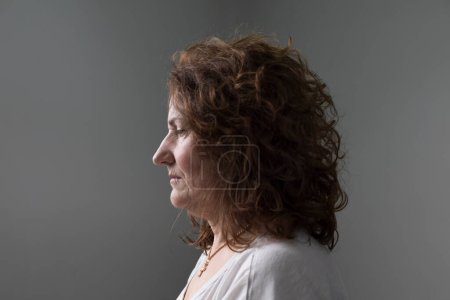 Retrato con fondo blanco de una mujer adulta de perfil con cabello castaño rizado. expresión seria