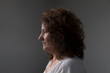 Retrato con fondo blanco de una mujer adulta de perfil con cabello castaño rizado. expresión seria