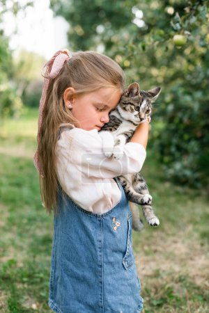 A pretty little girl with a bow on her head snuggled up to the cat