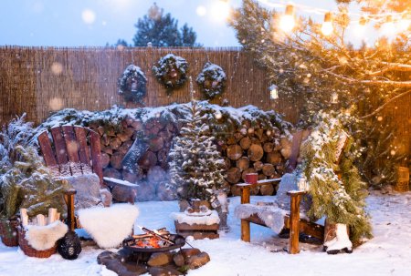 Foto de Decoración de Navidad en el patio: un árbol de Navidad con una guirnalda, sillas de madera junto al fuego, leña, coronas de Navidad - Imagen libre de derechos