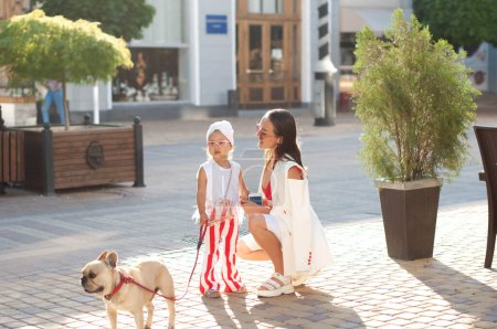 A young stylish mother with her daughter and her dog, a French bulldog, on a walk in the city. Family time