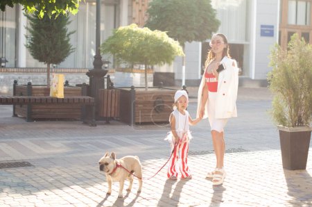 A young stylish mother with her daughter and her dog, a French bulldog, on a walk in the city. Family time