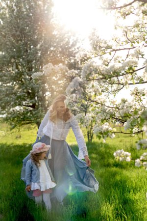 Foto de Una niña y su madre están caminando en el prado bajo una pera floreciente tre - Imagen libre de derechos