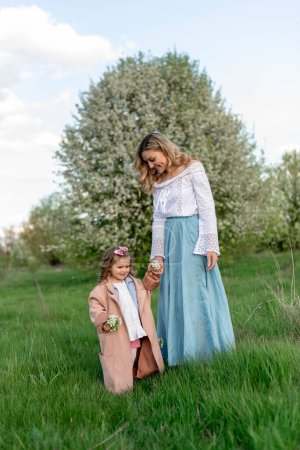 Eine Mutter mit einer kleinen Tochter auf einem Spaziergang zwischen einer grünen Wiese und einem blühenden Birnbaum