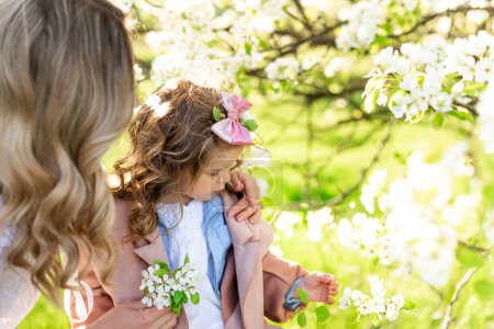 Foto de Una madre con una linda hijita cerca de un peral floreciente en un prado - Imagen libre de derechos
