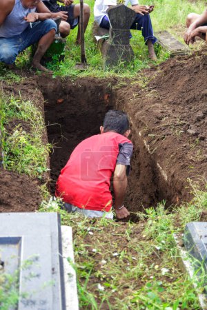 Photo for Yogyakarta, Indonesia. October 23, 2022: a man a red t-shirt is digging a grave at cemetery - Royalty Free Image