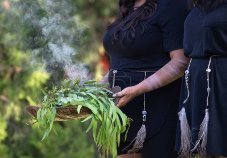 Téléchargez les photos : Cérémonie aborigène australienne de fumage, les mains de la femme tiennent des branches d'eucalyptus en feu, le rite rituel à l'événement communautaire, symbole de la culture et des traditions autochtones - en image libre de droit