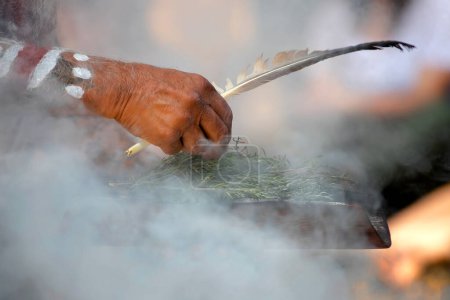 Foto de La mano humana sostiene el plato de madera y la pluma en el rito ritual del humo en un evento de la comunidad indígena en Australia - Imagen libre de derechos