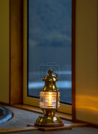 Une lanterne avec une lumière jaune chaud sur le fond d'une fenêtre pluvieuse dans une cabine de navire, un symbole de confort et de sécurité, image confortable