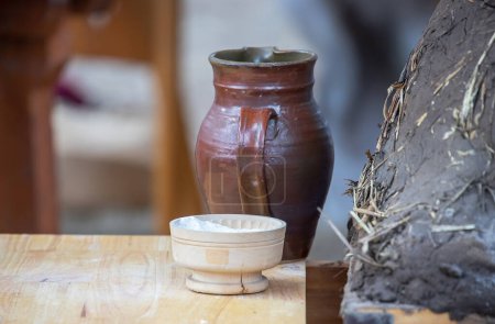 Jarra de cerámica, tazón con harina y horno de barro medieval para hornear pan de cerca, platos en una mesa de madera, estilo de vida medieval, bodegón. 