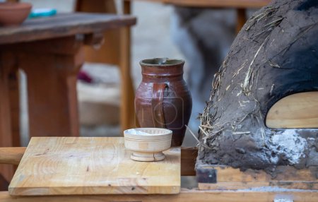 Pot en céramique, bol avec farine et four médiéval en argile pour la cuisson du pain close-up, vaisselle sur une table en bois, style de vie médiéval, nature morte. 