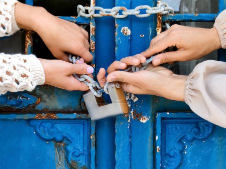 Photo for Womens hands are trying to break thick chain with padlock to open old door, close-up - Royalty Free Image