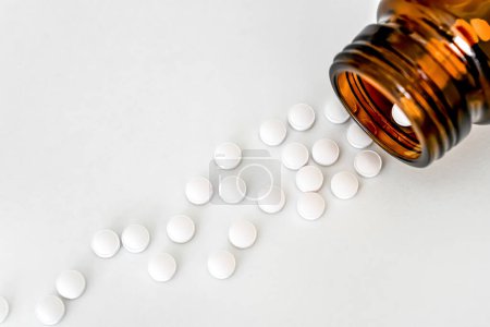 Medizin in Nahaufnahme: Weiße Pillen und braune Fläschchen auf weißem Tisch angeordnet, Nahaufnahme, flache Liege, Draufsicht, Kopierraum