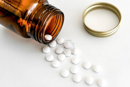 Verstreute weiße Pillen und braune Fläschchen, Nahaufnahme auf weißem Hintergrund, Konzept der Pharmazie