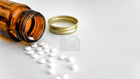 Téléchargez les photos : Pilules blanches dispersées avec bouteille en verre brun sur fond blanc, espace de copie, Gros plan, concept de soins de santé - en image libre de droit