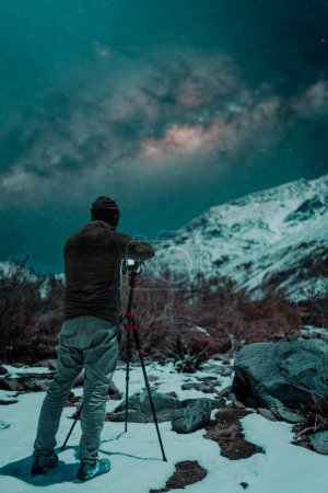 Téléchargez les photos : Photographe dans la neige la nuit prenant des photos des étoiles et de la voie lactée sur la montagne enneigée - en image libre de droit