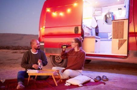 mid adult adventurous Caucasian couple having picnic in desert landscape with their camper trailer