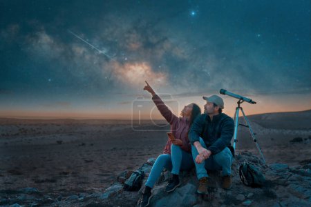 zwei Menschen, die in der Wüste sitzen und neben einem Teleskop die Sterne und die Milchstraße beobachten, Sternenbeobachtung und Erkundungskonzept 