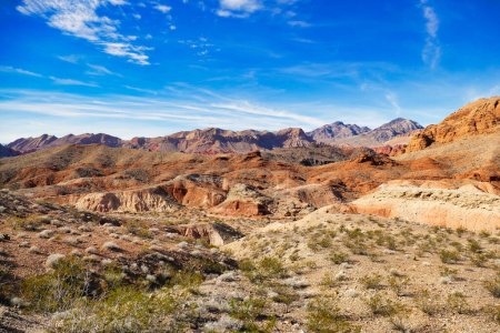 Foto de Paisaje árido desértico con rocas rojas erosionadas, vegetación escasa y montañas oscuras en el fondo, en Valley of Fire State Park, Nevada, EE.UU.. - Imagen libre de derechos