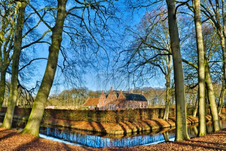 Téléchargez les photos : The 14-17th-century Manor House Menkemaborg, Uithuizen, Groningen, Netherlands, surrounded by a moat and old trees, on a sunny winter day, trees reflecting in the water - en image libre de droit