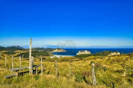 Téléchargez les photos : Stillez au-dessus d'une clôture le long de la promenade Clifftop, Cape Farewell, le point le plus au nord de l'île du Sud de la Nouvelle-Zélande. Vue panoramique sur la mer, les falaises, les forêts et les pâturages du parc agricole Puponga. - en image libre de droit