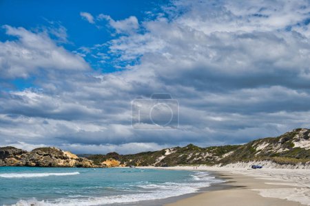 Téléchargez les photos : Plage tranquille sur une baie, avec des dunes et des rochers érodés, sous un ciel avec des nuages sombres. Voitures sur la plage. Nanarup Beach près d'Albany, Australie occidentale. - en image libre de droit