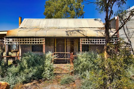 Téléchargez les photos : Chalet abandonné en fer ondulé et en bois, avec un jardin envahi, dans l'ancienne ville minière d'or de Kookynie, maintenant une ville fantôme, dans le shire de Menzies, en Australie occidentale - en image libre de droit