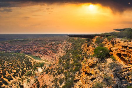 Foto de Las rocas rojas se iluminan bajo el ardiente atardecer sobre el desierto del Parque Nacional Kalbarri, Australia Occidental, el Skywalk sobre el cañón del río Murchison a la derecha. - Imagen libre de derechos