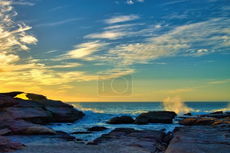 Téléchargez les photos : Coucher de soleil ardent au Mushroom Rock, parc national de Kalbarri, Australie-Occidentale, avec des vagues qui s'écrasent sur les rochers et des nuages orange tordus - en image libre de droit