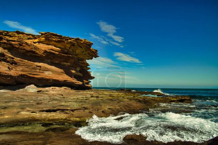 Heavily eroded red-brown sandstone cliffs and rock plateau with rock pools at the coast of Kalbarri National Park, Western Australia.