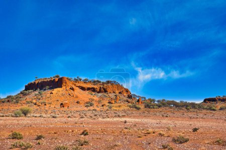 Formations de latérite rouge (roches avec fer et aluminium) entourées de buissons salés et de mulga dans le désert près du mont Magnet, Australie occidentale.