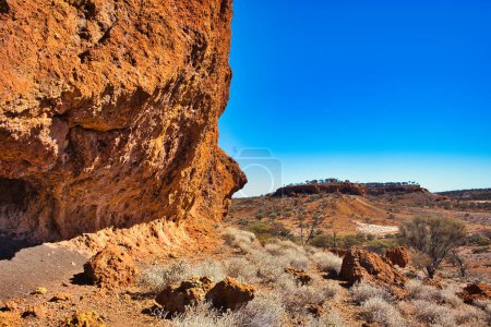 Roche de latérite rouge érodée et butte lointaine dans l'arrière-pays près du mont Magnet, dans le centre-ouest de l'Australie occidentale.