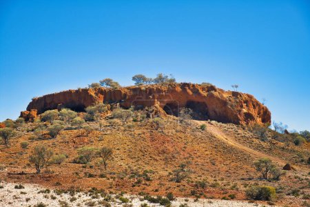 Stark erodiertes rotes Gestein mit einer riesigen Höhle und spärlicher Wüstenvegetation im westaustralischen Outback in der Nähe des Mount Magnet