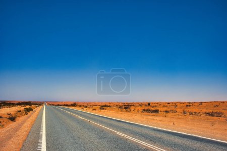 Foto de Autopista recta a través de un paisaje desolado de polvo y tierra roja en el interior de Australia Occidental, entre Exmouth y Coral Bay. - Imagen libre de derechos