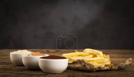 Photo for French fries with sauces on rustic wooden background. - Royalty Free Image