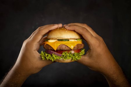 Hand hält einen Cheeseburger auf dunklem Hintergrund.