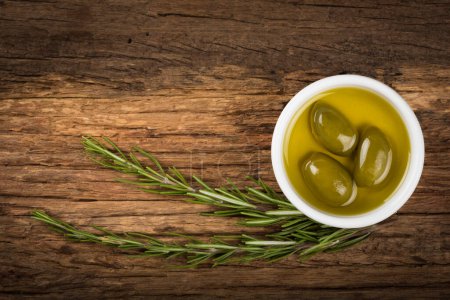Téléchargez les photos : Bol à l'huile d'olive vierge et olives vertes sur fond bois rustique. - en image libre de droit