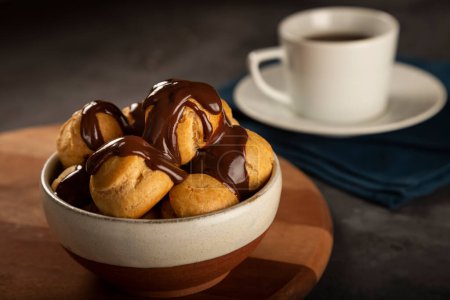Delicious profiteroles with coffee on the table.