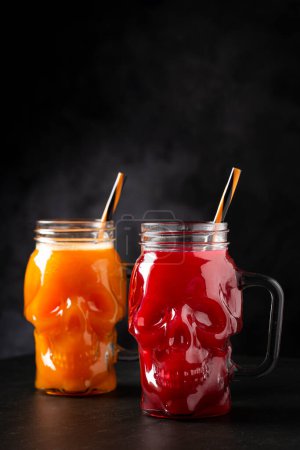 Halloween drink. Pumpkin drink and blood drink in skull glass.