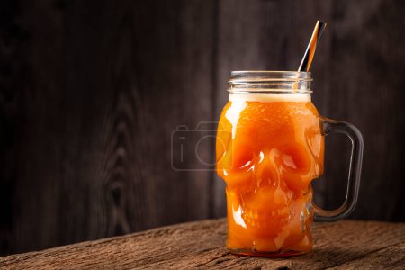 Halloween drink. Pumpkin drink in skull glass. Poster 709773662