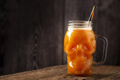 Halloween drink. Pumpkin drink in skull glass. Poster #709773662