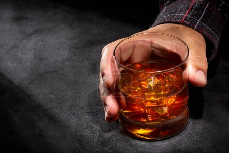 Hand hält Glas Whisky auf dunklem Hintergrund.