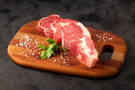 Foto de Carne ancha cruda lista para asar en una tabla de cortar de madera. - Imagen libre de derechos