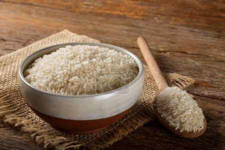 Photo for Raw white rice in a ceramic bowl on brown wooden background. - Royalty Free Image
